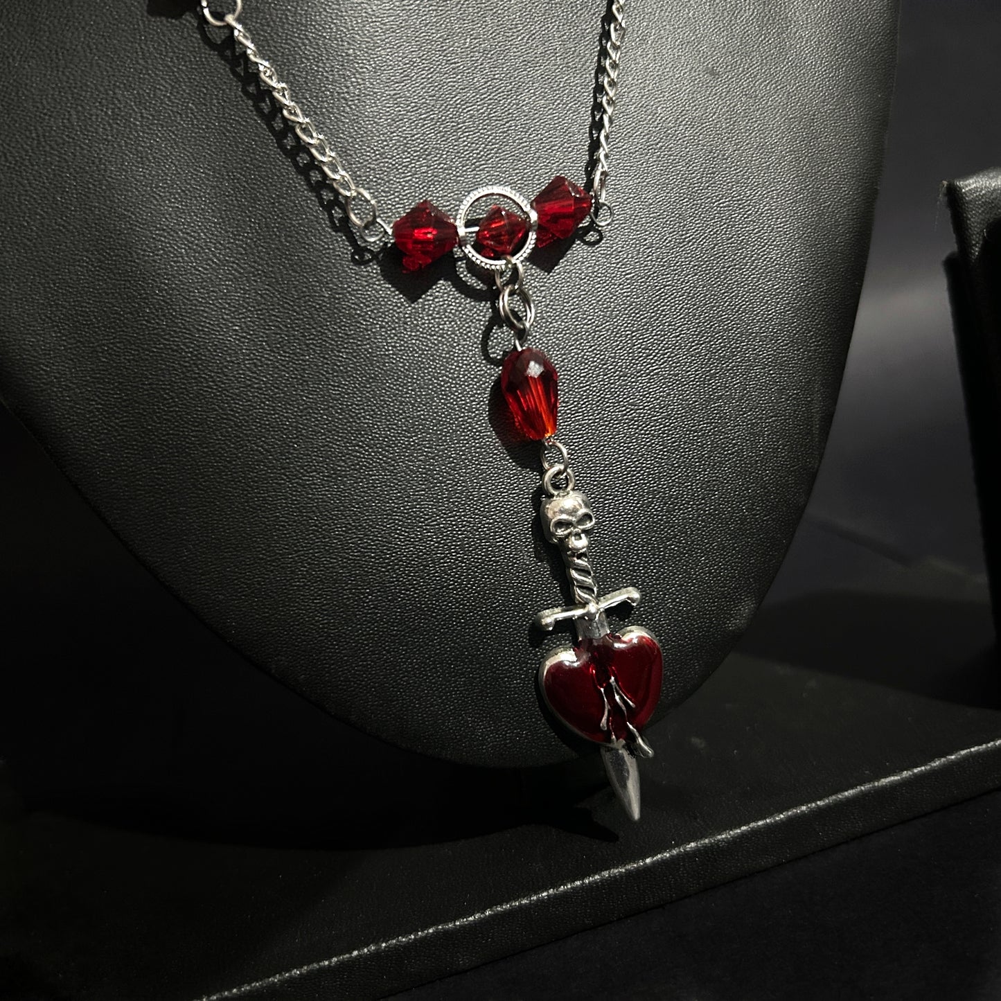 Angled close-up of dagger piercing heart pendant with red crystal details. Grunge gothic necklace for alt and punk fashion lovers in India.