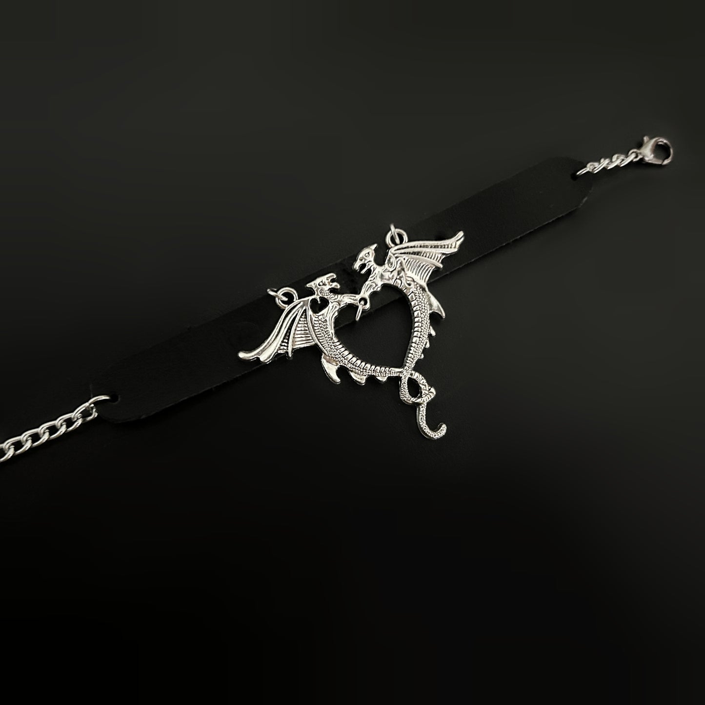 Flat lay of gothic black leather wrist cuff with silver dragons forming a heart-shaped centerpiece. Bold bracelet-cuff accessory design for fantasy, gothic, punk, alt, cosplay, and y2k inspired fashion in India
