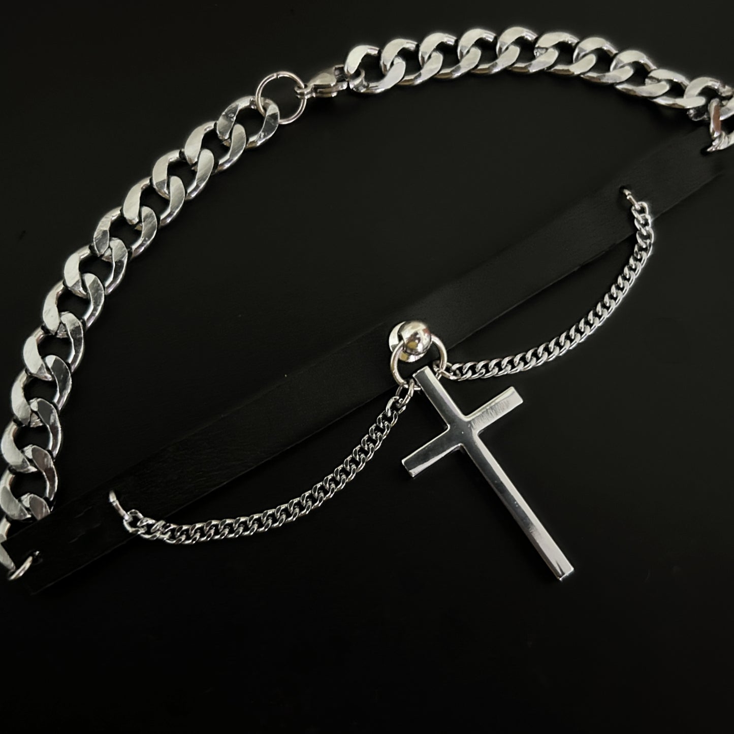 Overhead view of black leather punk rock-themed choker with large cross charm and silver chain. Stainless steel collar. Perfect for lovers of alt, grunge and y2k fashion across India.
