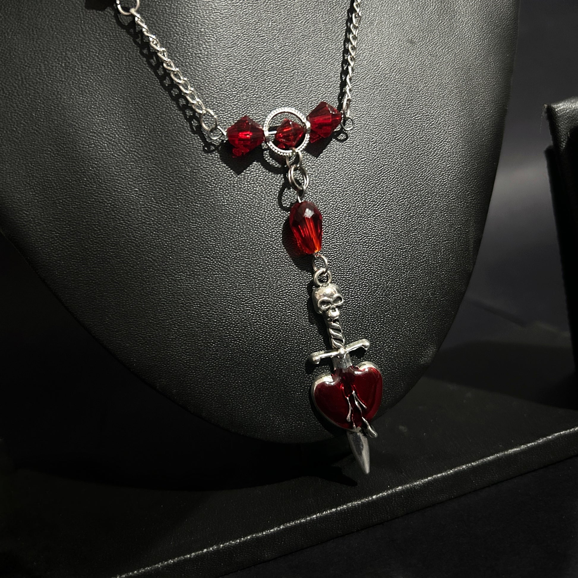 Angled close-up of dagger piercing heart pendant with red crystal details. Grunge gothic necklace for alt and punk fashion lovers in India.