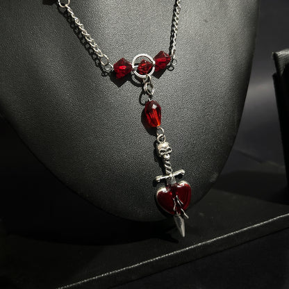 Angled close-up of dagger piercing heart pendant with red crystal details. Grunge gothic necklace for alt and punk fashion lovers in India.