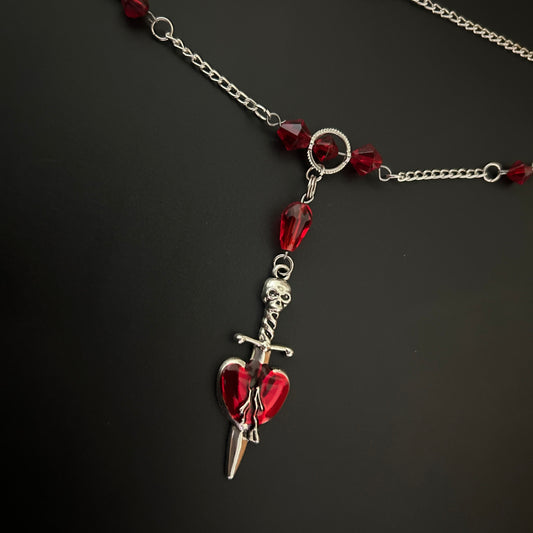 Flatlay of Crimson Heart Dagger Necklace with deep red stones and spear pendant. Gothic romance meets alt fashion jewelry.