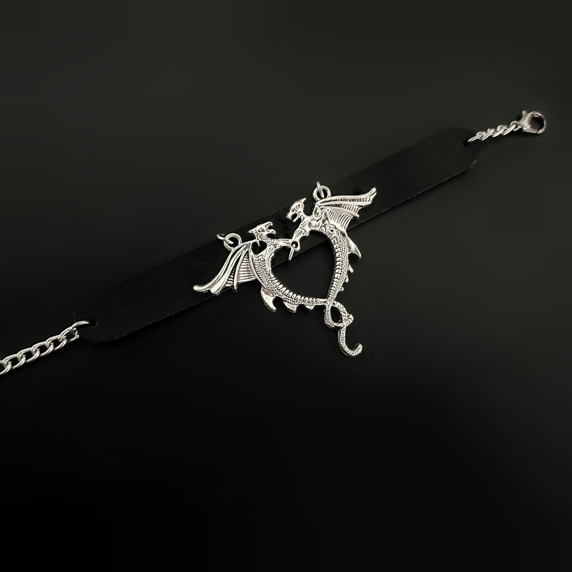 Flat lay of gothic black leather wrist cuff with silver dragons forming a heart-shaped centerpiece. Bold bracelet-cuff accessory design for fantasy, gothic, punk, alt, cosplay, and y2k inspired fashion in India
