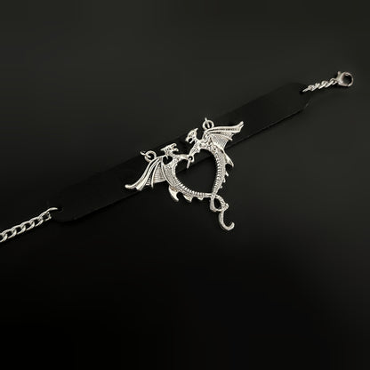 Flat lay of gothic black leather wrist cuff with silver dragons forming a heart-shaped centerpiece. Bold bracelet-cuff accessory design for fantasy, gothic, punk, alt, cosplay, and y2k inspired fashion in India
