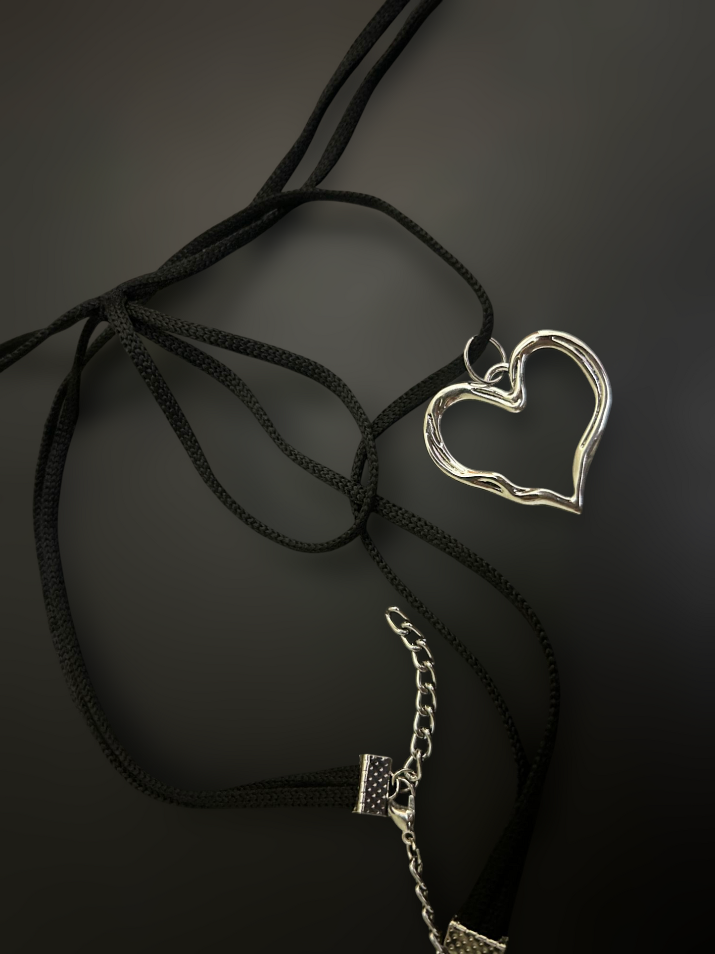 Flat lay of black nylon string choker with silver heart pendant and extender chain. Lightweight adjustable alt fashion piece. Phantom Cat India.