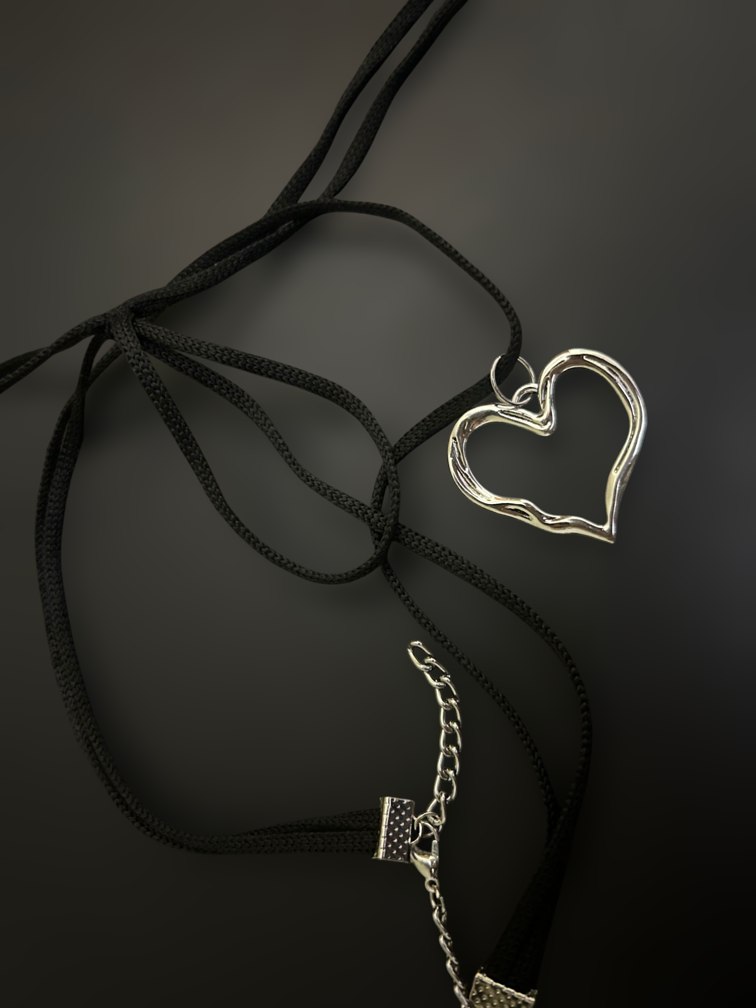 Flat lay of black nylon string choker with silver heart pendant and extender chain. Lightweight adjustable alt fashion piece. Phantom Cat India.