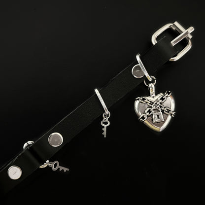 Flat lay of black leather choker with chained silver heart and padlock centerpiece, with stainless steel key charms. Gothic, alt, rockstar, and grunge jewelry by Phantom Cat India.