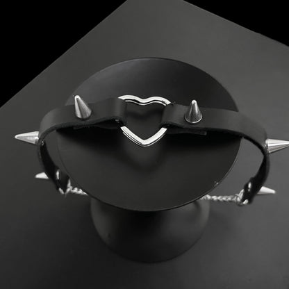 Top view flat lay of black leather gothic choker with bold conical spikes and a silver heart ring centerpiece, perfect for grunge jewelry lovers, Y2K styling, alt fashion, and cosplay outfits.